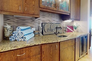 A kitchen with wooden cabinets, a granite countertop, and a decorative sign. - The Diamond Penthouse (Galveston)