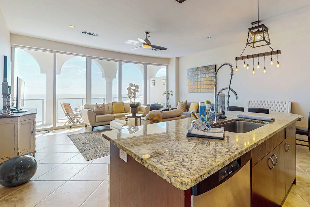 A spacious living area with a large island kitchen, a ceiling fan, and a view through large windows.