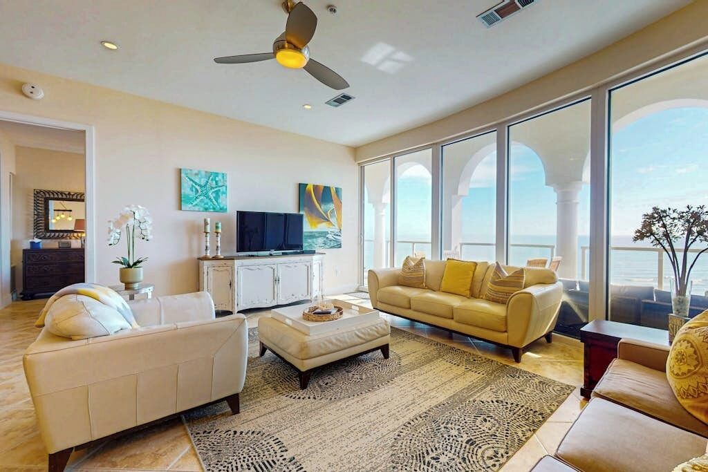A spacious living room with a large window, a ceiling fan, and a television.