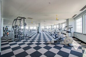 A gym with a checkered floor, various exercise equipment, and large windows allowing natural light. - The Diamond Penthouse (Galveston)