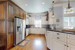 A kitchen with wooden cabinets, a stainless steel refrigerator, and a large island with a sink. - Fun In The Sun - Boat Slip, Pool & Sundeck (Corpus Christi)