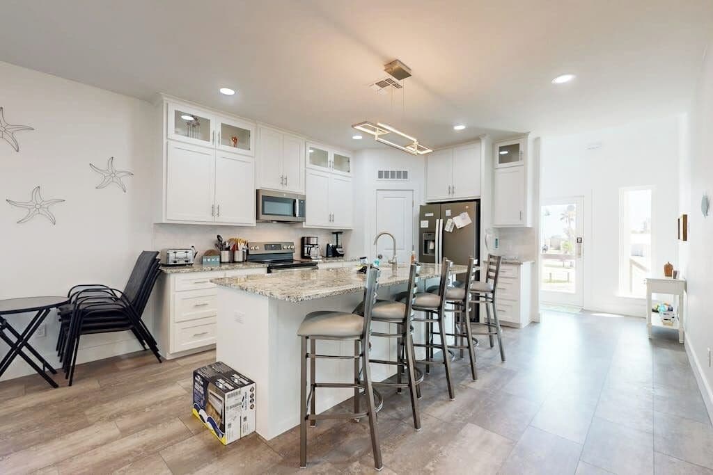 A modern kitchen with white cabinetry, a central island with bar stools, and a microwave.
