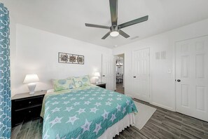Ein Schlafzimmer mit Bett, Nachttischen, Deckenventilator und einer Tür.
