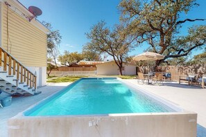 Ein rechteckiger Pool mit einer Holzterrasse und einer Treppe, die zu einem Gebäude führt.