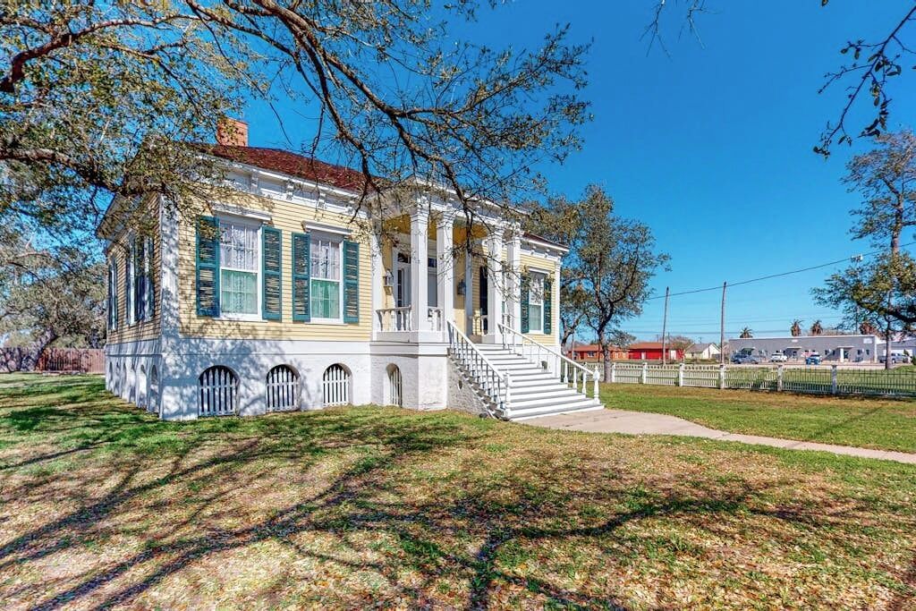 A historic building with a central staircase, columns, and a covered porch.