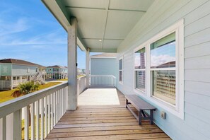 Eine überdachte Veranda mit Holzterrasse, weißen Geländern und einer Bank.