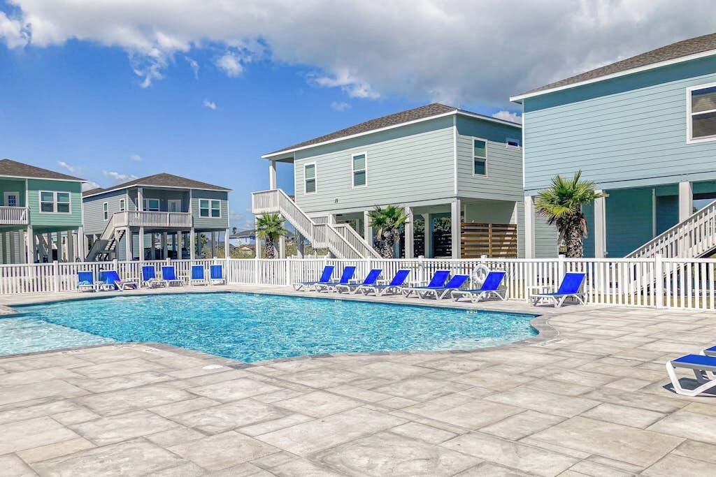A swimming pool with blue lounge chairs and a white fence.