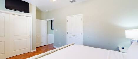 A bedroom with a bed, a ceiling fan, a TV mounted above the bed, and a nightstand with a lamp.