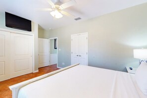 A bedroom with a bed, a ceiling fan, a TV mounted above the bed, and a nightstand with a lamp. - Marquesas 401 - Shared Pool, Patio & Dogs OK (Corpus Christi)