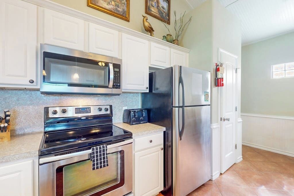 A kitchen with white cabinetry, a stainless steel refrigerator, a microwave, and a stove.