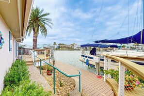 A marina with boats docked, a palm tree, and a wooden deck with railings. - Coral Cove - Waterfront with Amazing Views (Rockport)