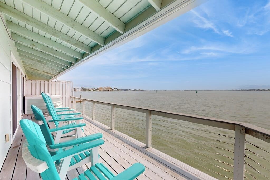 A covered deck with turquoise chairs overlooking a body of water.