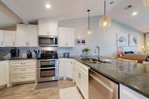 A modern kitchen with white cabinetry, stainless steel appliances, and a marble countertop. - Tranquil Turtle #503 (Rockport)