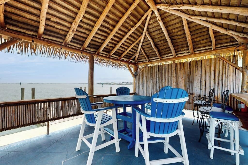 A covered outdoor seating area with a view of the water, featuring a table and chairs.