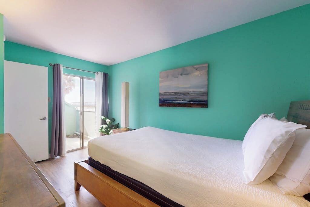 Ein Schlafzimmer mit einem Bett, einem Bild und Blick durch eine Tür.