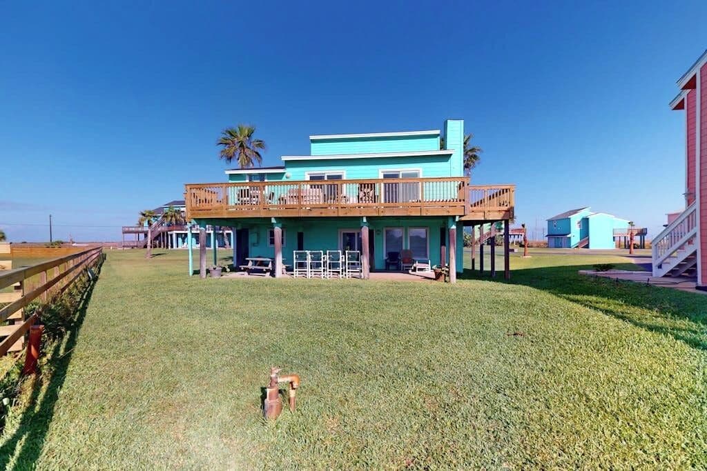 A two-story building with a balcony, a grassy lawn, and palm trees in the background.