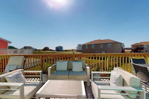 A deck with outdoor seating, a railing, and a view of buildings in the distance. - Seas the Day Getaway (Port Aransas)