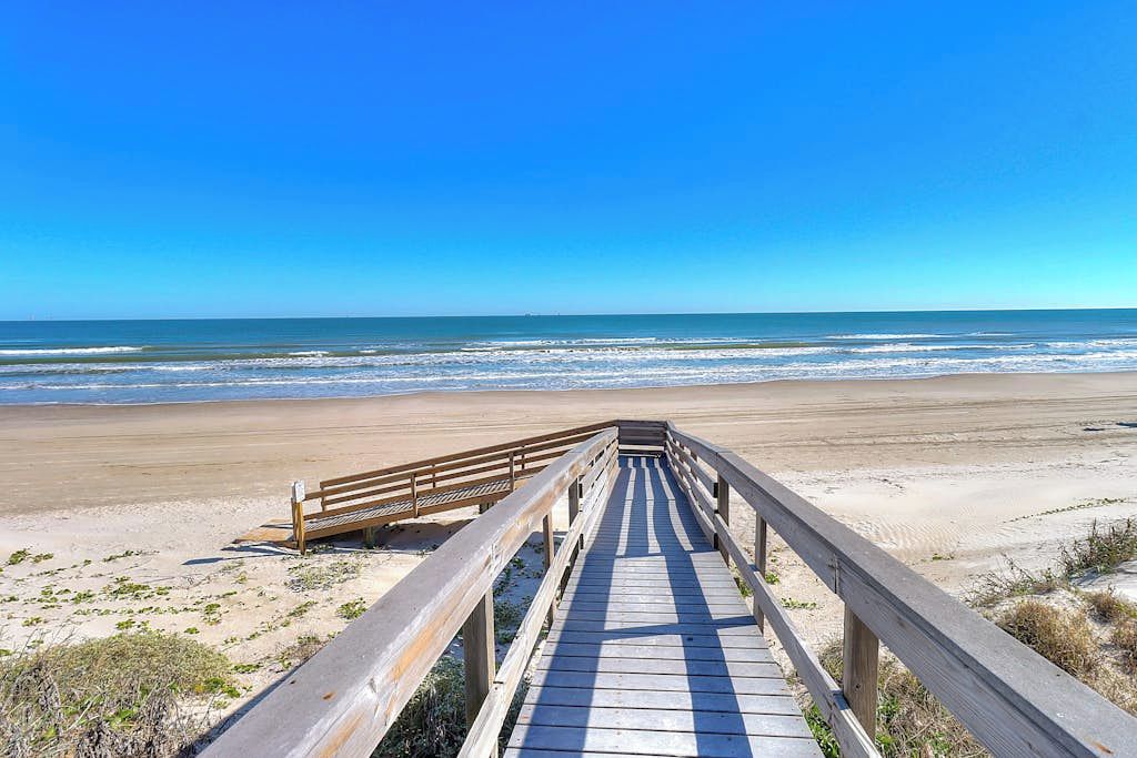 A wooden boardwalk leading to a sandy beach with a clear blue sky.