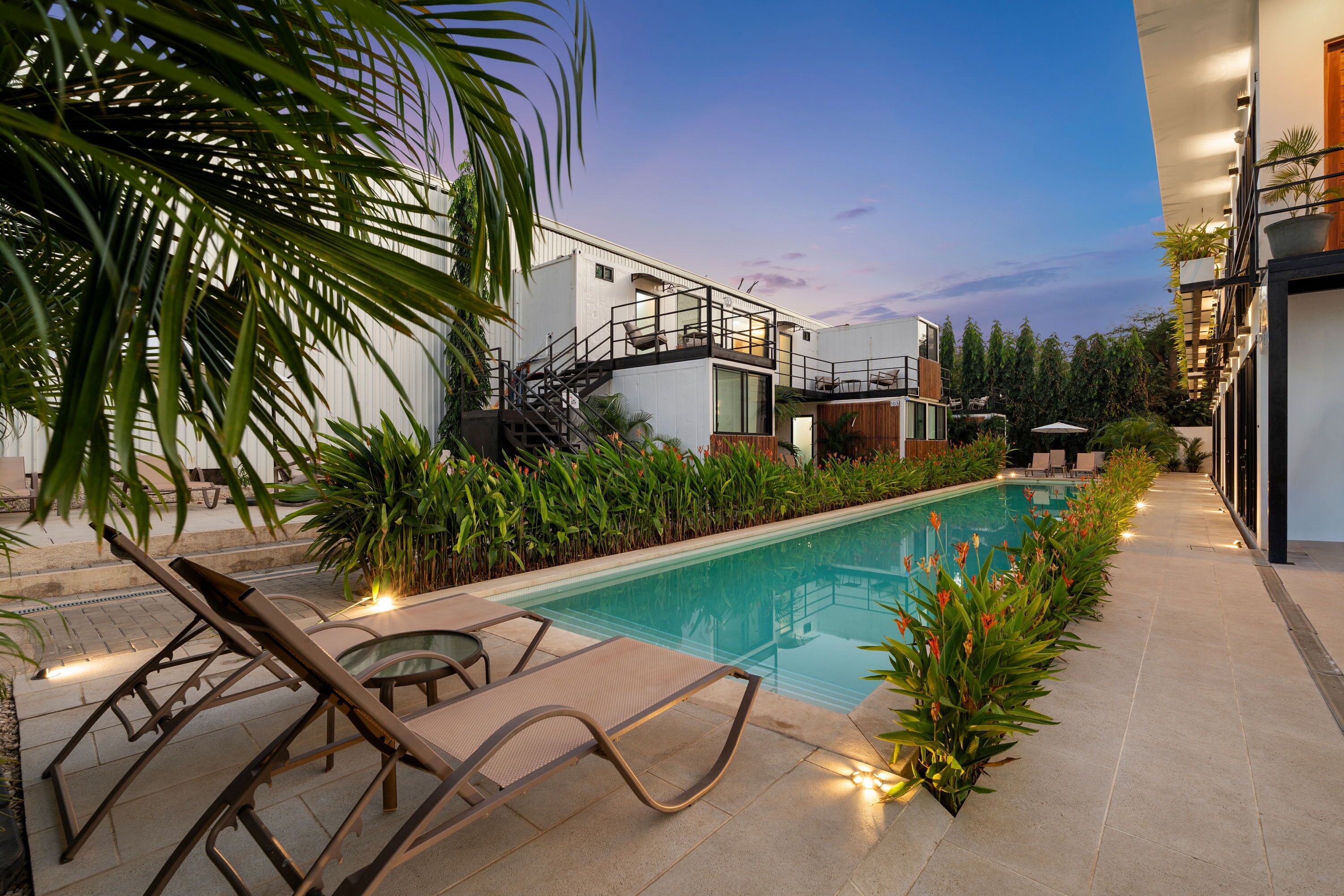 A modern outdoor pool area with lounge chairs, a staircase, and a building with a balcony.