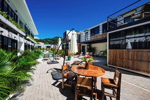 A courtyard with a wooden table and chairs, surrounded by potted plants and outdoor seating. - Luxury Nomad Containers (TAMARINDO)