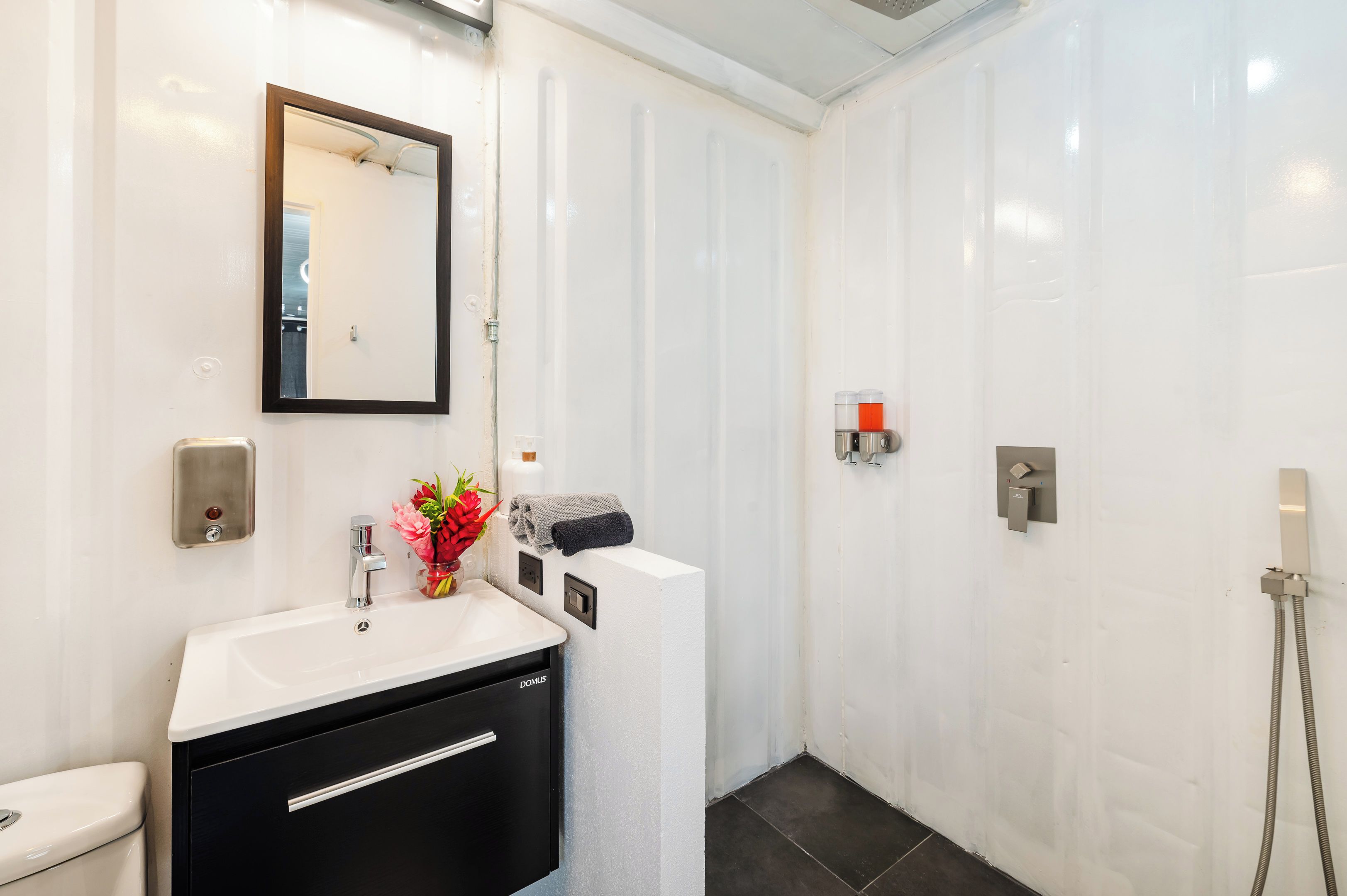 A modern bathroom with a white sink, a mirror, a toilet, and a shower area.