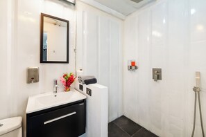 A modern bathroom with a white sink, a mirror, a toilet, and a shower area. - Luxury Nomad Containers (TAMARINDO)