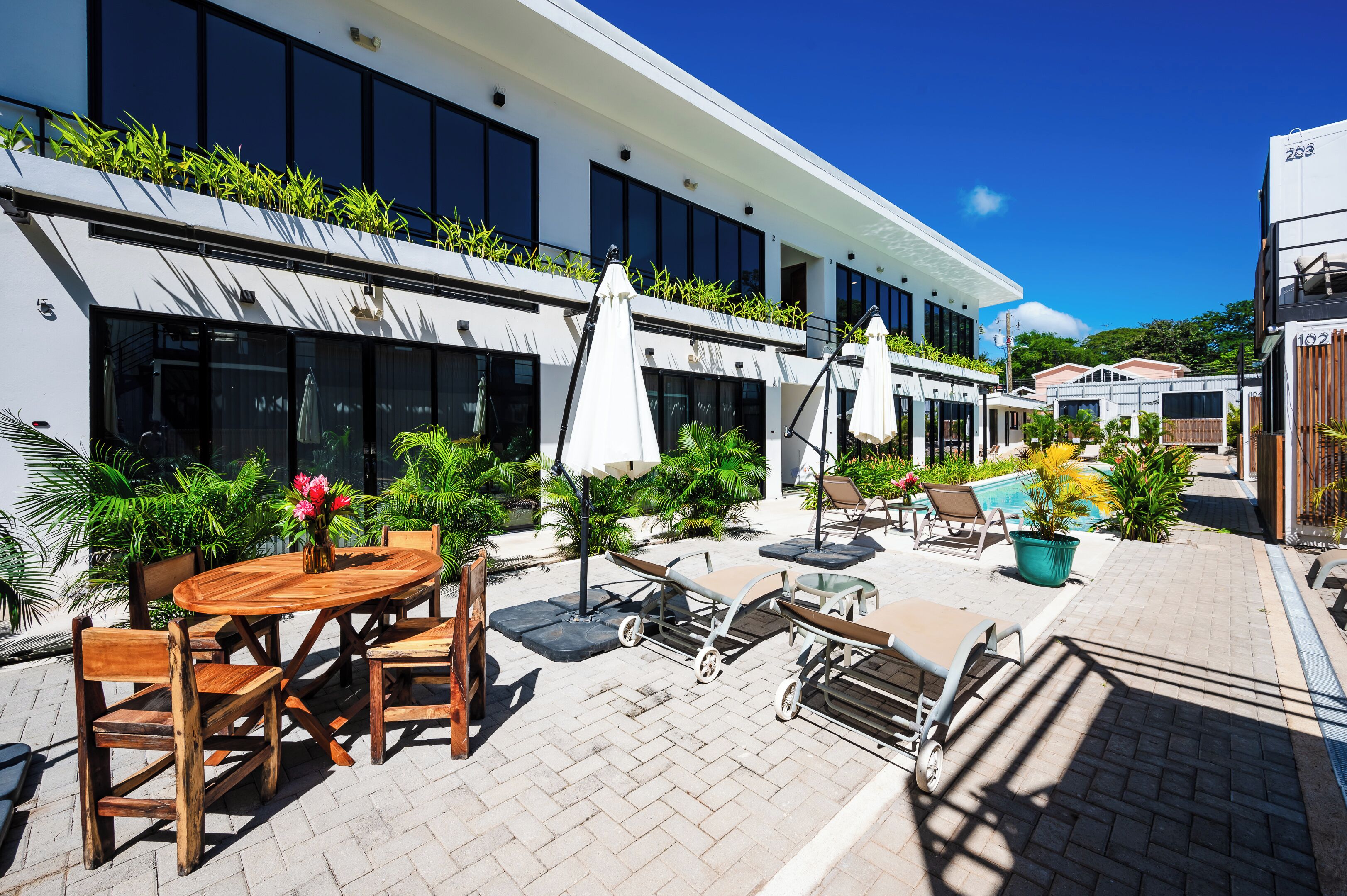 Un edificio moderno con un patio que cuenta con asientos al aire libre, sombrillas y plantas en macetas.