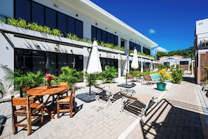 A modern building with a patio area featuring outdoor seating, umbrellas, and potted plants.
