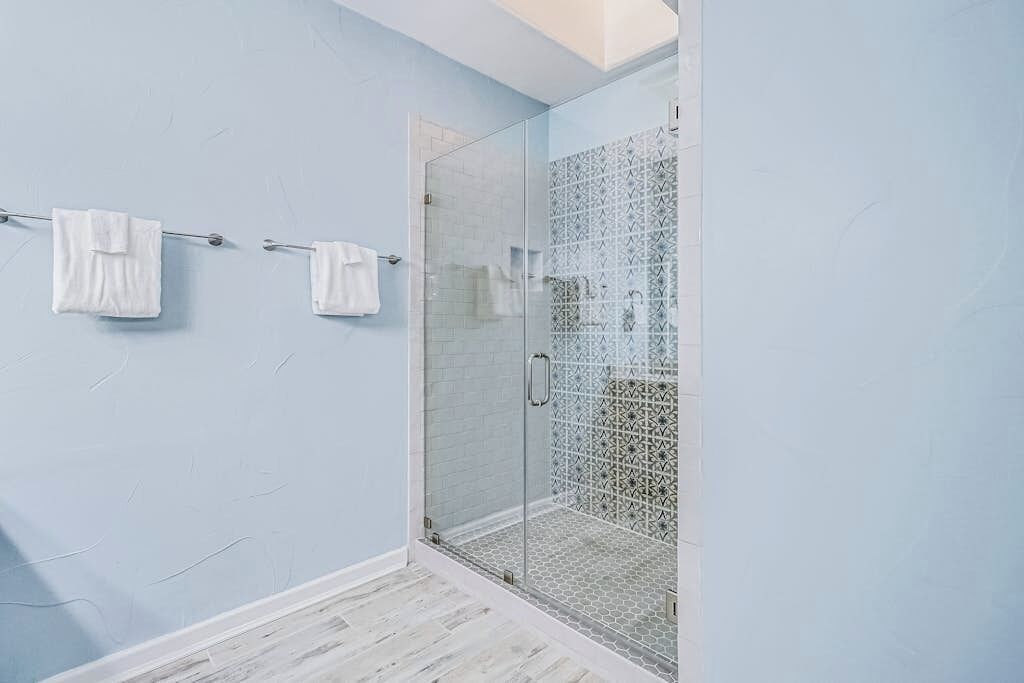 A bathroom with a glass shower enclosure, white towels on a rack, and a light blue wall.