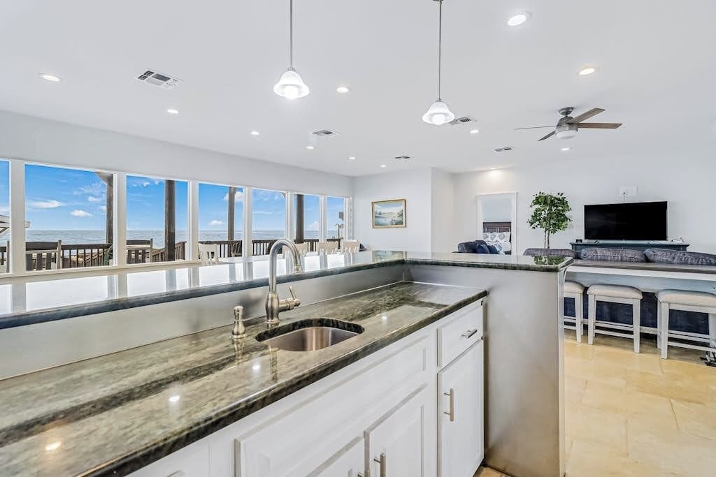 A modern kitchen with a large island, a built-in sink, pendant lighting, and a view of the ocean.