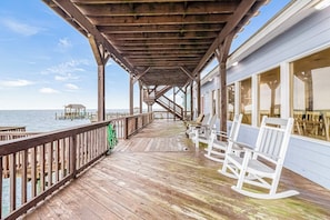 A wooden deck with a railing, white rocking chairs, and a view of the sea. - Bay Breeze Beauty - Waterfront, Hot Tub & Dogs OK (Rockport)