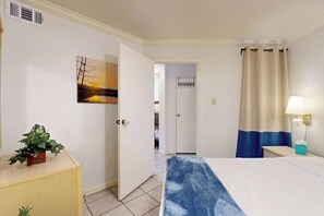 Ein Hotelzimmer mit Bett, Nachttisch, Lampe, Pflanze und einem Bild an der Wand.