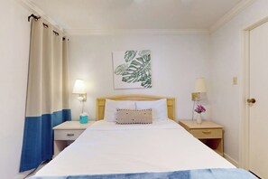 Une chambre d’hôtel avec un lit, des tables de chevet, une commode, une lampe, un tableau et une porte.