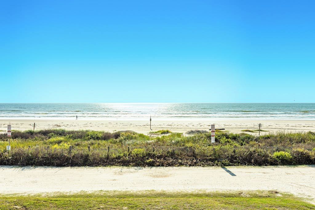 A beach with a clear sky, sandy shore, and a fence line.