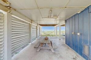 A covered outdoor area with a picnic table, a view of the beach, and a blue building in the background. - Seas the Day - Beachfront, Panoramic Gulf Views (Galveston)