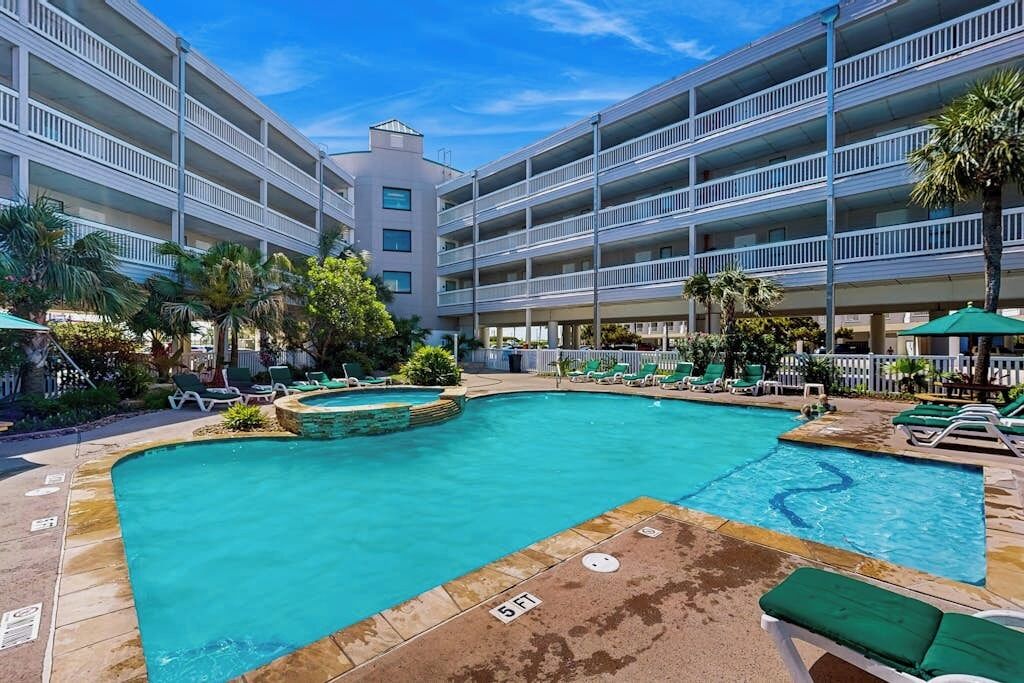 A hotel with a swimming pool, multiple balconies, and lounge chairs.