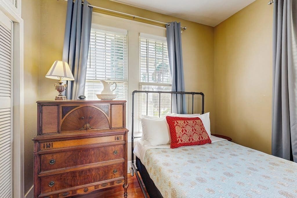 A bedroom with a bed, a dresser, and a window with curtains.