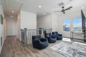 A spacious living area with a high ceiling, a ceiling fan, and a large window providing a view of the outside. - Sky Blue Shores - Gulf Views, Decks, Sleeps 16 (Galveston)