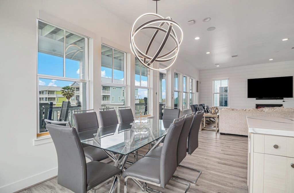 A modern dining area with a glass table and chairs, large windows, and a contemporary light fixture.