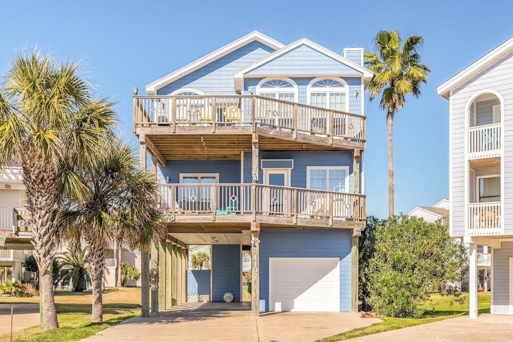 A two-story residential building with a balcony on the upper floor, a garage, and a clear sky.