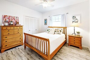 Ein Schlafzimmer mit einem hölzernen Bett, einem Schminktisch, einem Nachttisch und einem Deckenventilator.