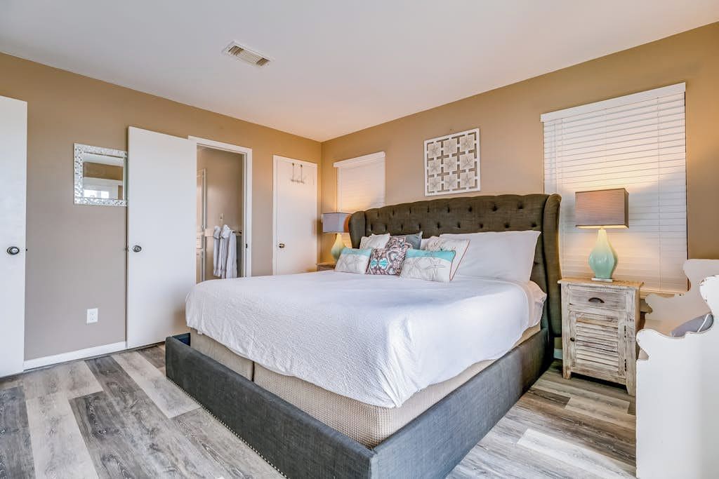 A bedroom with a large bed, a bedside table, a lamp, and a mirror on the wall.