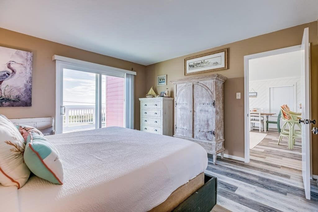 Une chambre à coucher avec un lit, une commode, un tableau et une vue sur un balcon.