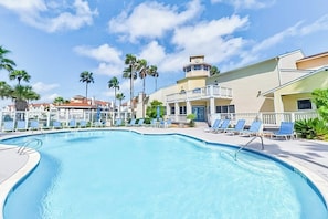 A swimming pool with lounge chairs and palm trees. - Beach Club - Ocean Breeze Retreat – Island Condo (Corpus Christi)