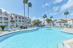 Ein Swimmingpool mit Liegestühlen und Palmen, umgeben von Hotelgebäuden.