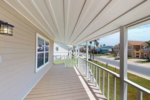 A covered porch with a railing, a window, and a view of a street with houses. - Padre Island Paradise on Hibiscus (South Padre Island)