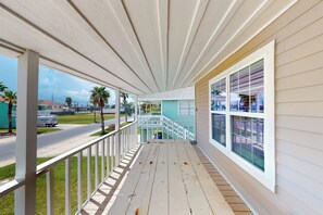 Eine überdachte Veranda mit Geländer, eine Treppe zu einer zweiten Ebene und Blick auf die Straße.