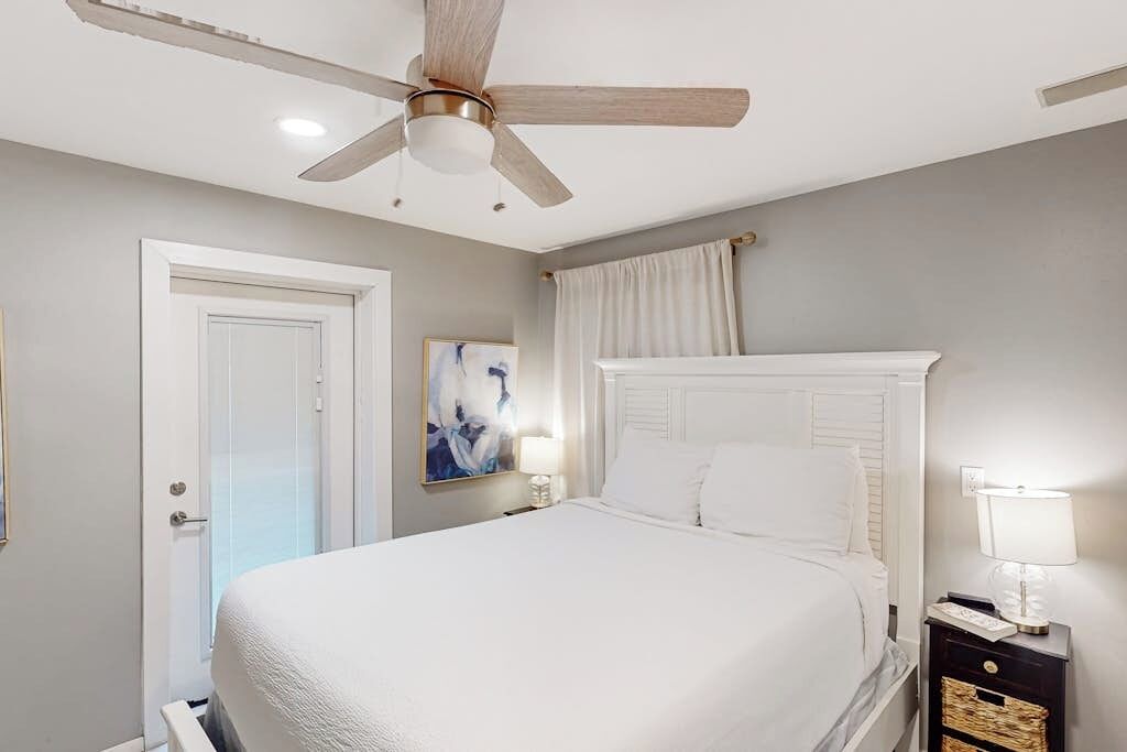 A bedroom with a bed, a ceiling fan, a nightstand, and a door.
