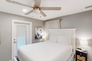 Un dormitorio con cama, ventilador de techo, mesita de noche y una puerta.