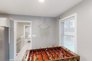 Ein Zimmer mit Tischfußball, einer hängenden Dekoration und einem Fenster mit Jalousien.
